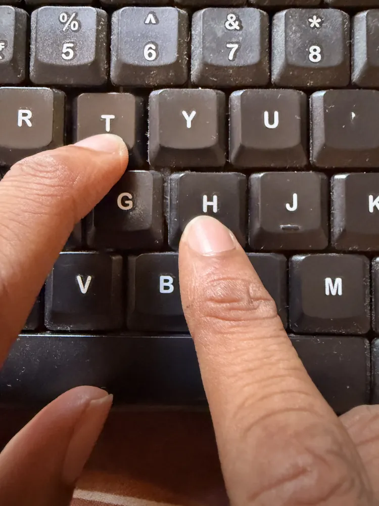 Close-up of hands demonstrating rolling finger movement between the T, H, and nearby keys during touch typing.